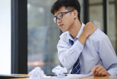 Boyun ağrısı ve yorgunluk çeken yorgun işadamı masasında otururken aşırı çalışma ve iş baskısı yüzünden stresli hissediyor..