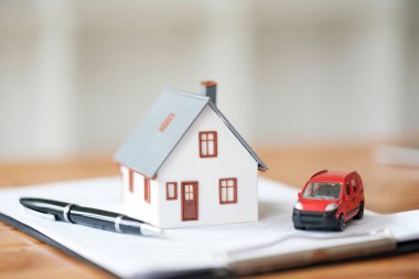 Kontrata konan minyatür ev ve araba modelleri, emlak işlemleri, araç satın alma anlaşmaları ve mülk sahipliği anlaşmalarını temsil ediyor.