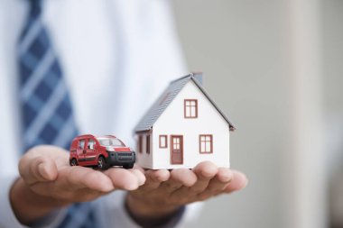 El ele tutuşan araba ve ev. Ev kredisi, araba sigortası, aile yaşam sigortası koruma, ev inşası için finansal ipotek ve miras planlama yatırım kavramı.