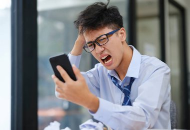 Sinirli iş adamı masasında çalışırken öfke ve stresi ifade ediyor. Bilgisayarına bağırıyor, iş sorunları, iş stresi ya da proje başarısızlığı yüzünden buruşuk kağıtlarla çevrili..