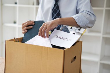 Bir işadamı kişisel eşyalarını bir kutuya koyarken görülüyor, muhtemelen istifa ettikten ya da işini kaybettikten sonra. Görüntü kariyer geçişlerini, işten çıkarmaları ya da bir rolden ayrılmayı simgeliyor..