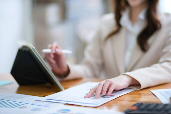 A businesswoman is reviewing charts and analyzing data while using a tablet. The image highlights focus on financial analysis, decision-making, and business strategy in a modern office setting.