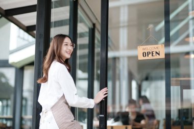 Bir kafe çalışanı, bir mağaza çalışanı ya da müşterileri karşılamak için kapıyı açan bir mal sahibi. Sahne, bir kafe ortamında samimiyet, konukseverlik ve profesyonelliğin sergilendiği yeni bir iş gününün başlangıcını vurguluyor..