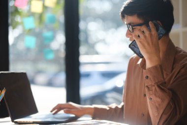 Bir iş adamı, tablet kullanırken ve finansal belgeleri incelerken, kurumsal iletişimi ve stratejik karar verme mekanizmasını temsil ederken bir telefon danışmanlığı yapıyor..