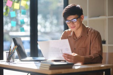 Yatırım kararları için mali verileri ve eğilimleri analiz eden genç bir işadamı. Odaklanmış ifadesi stratejik düşünme, iş planlaması ve finans ve eğitim yoluyla büyümeyi yansıtıyor..