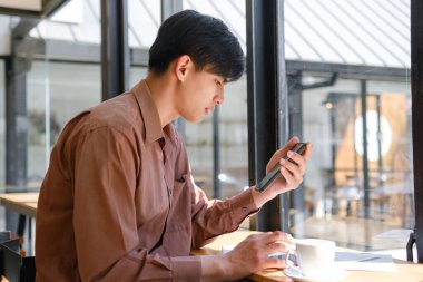 Bir kafede telefon mesajlarını kontrol ederken uzaktan çalışan bir işadamı. Bağlı ve üretken kalıyor, günlük ortamlarda iş ve rahatlığı dengeliyor..