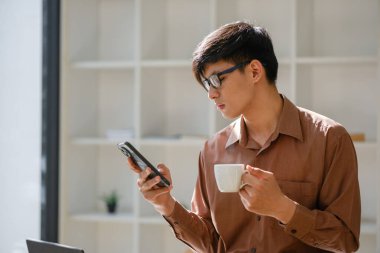 Bir iş adamı mola sırasında telefonunu kontrol ederken gülümsüyor ve elinde kahve fincanı tutuyordu. Bağlı kalarak bir anlık rahatlamanın tadını çıkarıyor..