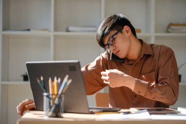 Bir iş adamı, tablet kullanırken ve finansal belgeleri incelerken, kurumsal iletişimi ve stratejik karar verme mekanizmasını temsil ederken bir telefon danışmanlığı yapıyor..