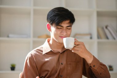 Genç bir adam sert bir fincan kahveyi tadıyor ve yoğun lezzetine tepki veriyor. Yoğun bir iş gününde kısa bir mola verirken kafein takviyesinin tadını çıkarmak..