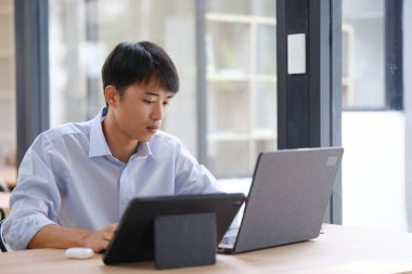 Hem tablet hem de dizüstü bilgisayarla çalışan bir işadamı, mali verileri, yatırım raporlarını veya iş stratejilerini analiz ediyor. Uzak çalışma veya danışmanlık için dijital araçlar kullanılıyor.