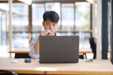 Odaklanmış bir iş danışmanı dizüstü bilgisayar üzerinde çalışıyor, mali verileri ve yatırım raporlarını analiz ediyor. Yoğunlaştırılmış ifadesi stratejik planlama, muhasebe veya piyasa araştırması öneriyor..