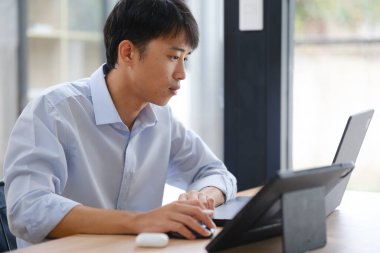 Hem tablet hem de dizüstü bilgisayarla çalışan bir işadamı, mali verileri, yatırım raporlarını veya iş stratejilerini analiz ediyor. Uzak çalışma veya danışmanlık için dijital araçlar kullanılıyor.