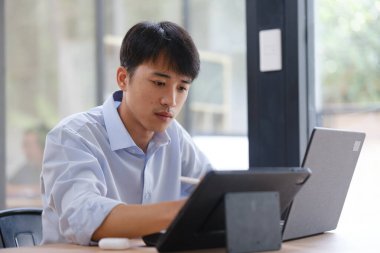 Hem tablet hem de dizüstü bilgisayarla çalışan bir işadamı, mali verileri, yatırım raporlarını veya iş stratejilerini analiz ediyor. Uzak çalışma veya danışmanlık için dijital araçlar kullanılıyor.