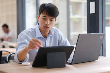 Hem tablet hem de dizüstü bilgisayarla çalışan bir işadamı, mali verileri, yatırım raporlarını veya iş stratejilerini analiz ediyor. Uzak çalışma veya danışmanlık için dijital araçlar kullanılıyor.