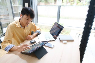 Sınavlara hazırlanmak için çevrimiçi öğrenim gören, notlar alan ve çalışma materyallerini kitaplarla ve dijital cihazlarla inceleyen bir öğrenci.