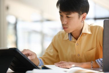 Sınavlara hazırlanmak için çevrimiçi öğrenim gören, notlar alan ve çalışma materyallerini kitaplarla ve dijital cihazlarla inceleyen bir öğrenci.