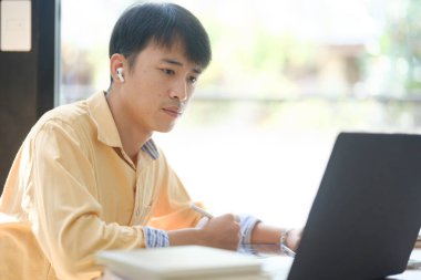 Sınavlara hazırlanmak için çevrimiçi öğrenim gören, notlar alan ve çalışma materyallerini kitaplarla ve dijital cihazlarla inceleyen bir öğrenci.