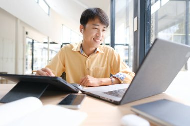 Sınavlara hazırlanmak için çevrimiçi öğrenim gören, notlar alan ve çalışma materyallerini kitaplarla ve dijital cihazlarla inceleyen bir öğrenci.