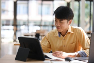 Sınavlara hazırlanmak için çevrimiçi öğrenim gören, notlar alan ve çalışma materyallerini kitaplarla ve dijital cihazlarla inceleyen bir öğrenci.