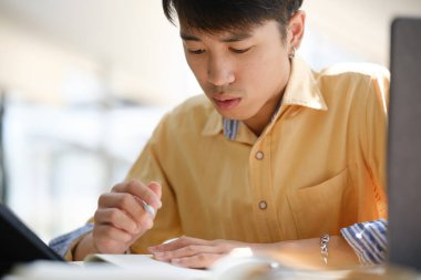 Sınavlara hazırlanmak için çevrimiçi öğrenim gören, notlar alan ve çalışma materyallerini kitaplarla ve dijital cihazlarla inceleyen bir öğrenci.