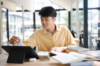 Sınavlara hazırlanmak için çevrimiçi öğrenim gören, notlar alan ve çalışma materyallerini kitaplarla ve dijital cihazlarla inceleyen bir öğrenci.