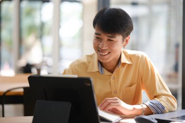 Sınavlara hazırlanmak için çevrimiçi öğrenim gören, notlar alan ve çalışma materyallerini kitaplarla ve dijital cihazlarla inceleyen bir öğrenci.