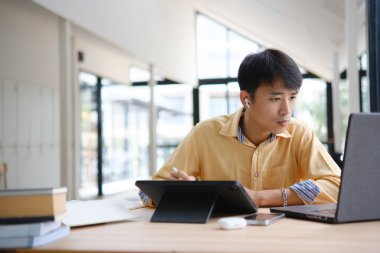 Sınavlara hazırlanmak için çevrimiçi öğrenim gören, notlar alan ve çalışma materyallerini kitaplarla ve dijital cihazlarla inceleyen bir öğrenci.