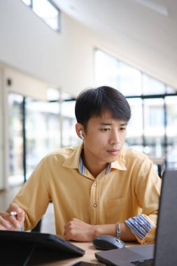 Sınavlara hazırlanmak için çevrimiçi öğrenim gören, notlar alan ve çalışma materyallerini kitaplarla ve dijital cihazlarla inceleyen bir öğrenci.