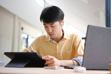 Sınavlara hazırlanmak için çevrimiçi öğrenim gören, notlar alan ve çalışma materyallerini kitaplarla ve dijital cihazlarla inceleyen bir öğrenci.