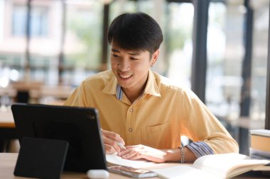 Sınavlara hazırlanmak için çevrimiçi öğrenim gören, notlar alan ve çalışma materyallerini kitaplarla ve dijital cihazlarla inceleyen bir öğrenci.