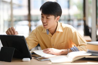 Sınavlara hazırlanmak için çevrimiçi öğrenim gören, notlar alan ve çalışma materyallerini kitaplarla ve dijital cihazlarla inceleyen bir öğrenci.