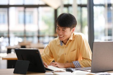 Sınavlara hazırlanmak için çevrimiçi öğrenim gören, notlar alan ve çalışma materyallerini kitaplarla ve dijital cihazlarla inceleyen bir öğrenci.