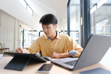 Sınavlara hazırlanmak için çevrimiçi öğrenim gören, notlar alan ve çalışma materyallerini kitaplarla ve dijital cihazlarla inceleyen bir öğrenci.