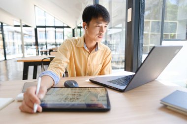 Sınavlara hazırlanmak için çevrimiçi öğrenim gören, notlar alan ve çalışma materyallerini kitaplarla ve dijital cihazlarla inceleyen bir öğrenci.