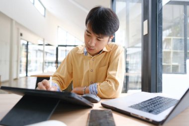 Sınavlara hazırlanmak için çevrimiçi öğrenim gören, notlar alan ve çalışma materyallerini kitaplarla ve dijital cihazlarla inceleyen bir öğrenci.