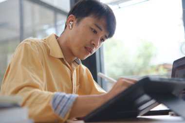 Sınavlara hazırlanmak için çevrimiçi öğrenim gören, notlar alan ve çalışma materyallerini kitaplarla ve dijital cihazlarla inceleyen bir öğrenci.