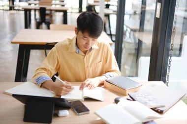 Sınavlara hazırlanmak için çevrimiçi öğrenim gören, notlar alan ve çalışma materyallerini kitaplarla ve dijital cihazlarla inceleyen bir öğrenci.