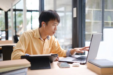 Sınavlara hazırlanmak için çevrimiçi öğrenim gören, notlar alan ve çalışma materyallerini kitaplarla ve dijital cihazlarla inceleyen bir öğrenci.