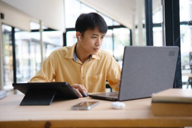 Sınavlara hazırlanmak için çevrimiçi öğrenim gören, notlar alan ve çalışma materyallerini kitaplarla ve dijital cihazlarla inceleyen bir öğrenci.