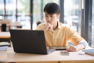 Sınavlara hazırlanmak için çevrimiçi öğrenim gören, notlar alan ve çalışma materyallerini kitaplarla ve dijital cihazlarla inceleyen bir öğrenci.