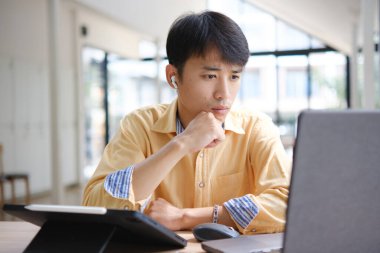 Sınavlara hazırlanmak için çevrimiçi öğrenim gören, notlar alan ve çalışma materyallerini kitaplarla ve dijital cihazlarla inceleyen bir öğrenci.