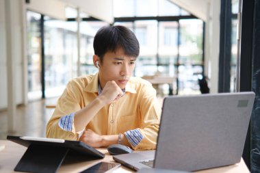 Sınavlara hazırlanmak için çevrimiçi öğrenim gören, notlar alan ve çalışma materyallerini kitaplarla ve dijital cihazlarla inceleyen bir öğrenci.