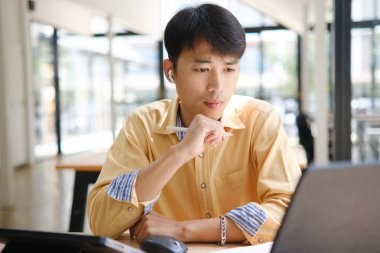 Sınavlara hazırlanmak için çevrimiçi öğrenim gören, notlar alan ve çalışma materyallerini kitaplarla ve dijital cihazlarla inceleyen bir öğrenci.