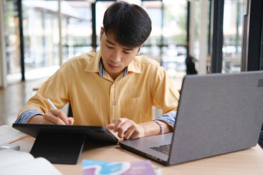 Sınavlara hazırlanmak için çevrimiçi öğrenim gören, notlar alan ve çalışma materyallerini kitaplarla ve dijital cihazlarla inceleyen bir öğrenci.