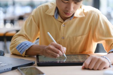 Sınavlara hazırlanmak için çevrimiçi öğrenim gören, notlar alan ve çalışma materyallerini kitaplarla ve dijital cihazlarla inceleyen bir öğrenci.