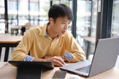 Sınavlara hazırlanmak için çevrimiçi öğrenim gören, notlar alan ve çalışma materyallerini kitaplarla ve dijital cihazlarla inceleyen bir öğrenci.