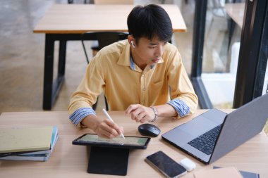 Sınavlara hazırlanmak için çevrimiçi öğrenim gören, notlar alan ve çalışma materyallerini kitaplarla ve dijital cihazlarla inceleyen bir öğrenci.