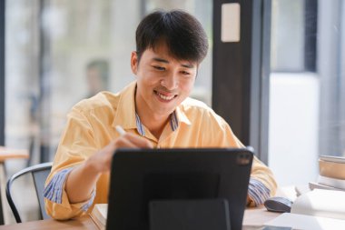 Sınavlara hazırlanmak için çevrimiçi öğrenim gören, notlar alan ve çalışma materyallerini kitaplarla ve dijital cihazlarla inceleyen bir öğrenci.