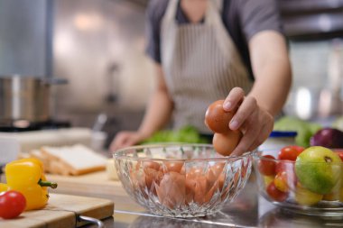 Mutfak tezgahındaki cam bir kaseden taze meyve ve sebzelerle çevrili kahverengi yumurtaları seçen şefin elini kapatın..