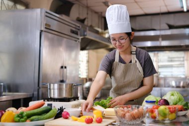 Bir şef, sağlıklı yemek hazırlamak için organik malzemeler kullanarak temiz yemek ve çiftlikten masaya yaklaşımı temsil eden ticari bir mutfakta sebze hazırlar..